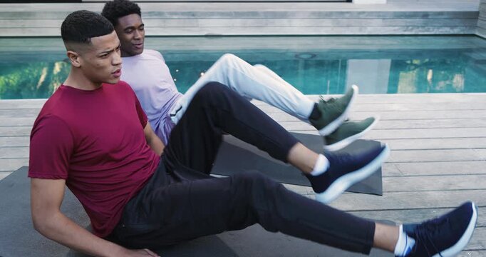 After flutter kicks on mats, diverse male friends high-fiving, chatting and breathing beside pool