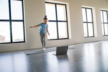 Child practicing balance and coordination at home on a yoga mat using a laptop