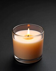 Lit candle in a clear glass container on a dark surface
