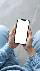 A top view of a man sits indoors and holds a smartphone with a white screen mockup. Mobile device mockup for app or UI design.
