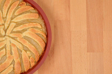 An apple pie with a decorative crust is shown in a red baking dish on a light wooden surface with ample copy space