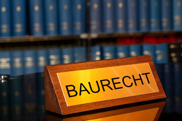 Symbolbild Baurecht: Messingschild mit der Aufschrift Baurecht vor einem großen Bücherregal...