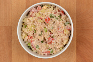 A white bowl brimming with a creamy salad of barley, peppers, tomatoes, and green onions, all mixed...