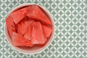 A white bowl brimming with refreshing red watermelon pieces is positioned on a patterned green and...