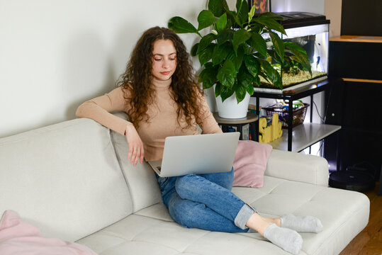 A young woman is comfortably working on her laptop at home, surrounded by various indoor plants