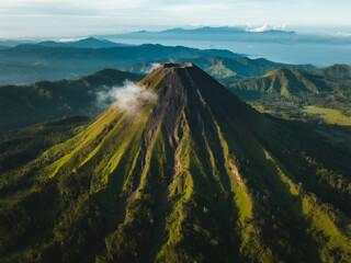 A mountain with a green peak and a cloud of smoke coming from it