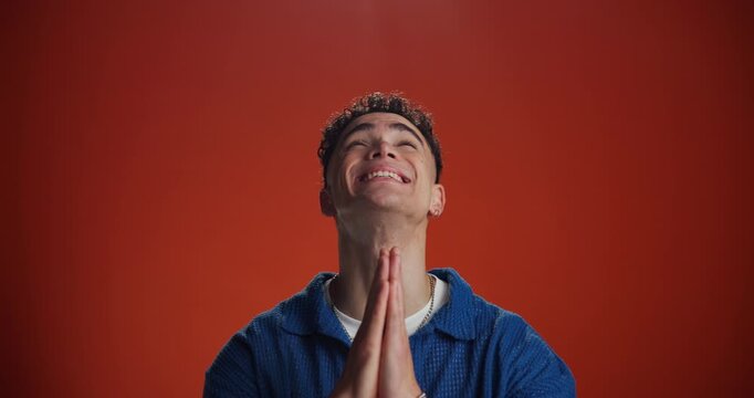 Scared, man and beg with praying in studio for desperate plea, anxiety and request for help. Mockup space, person and hope for assistance, spiritual stress or trust God for guidance on red background