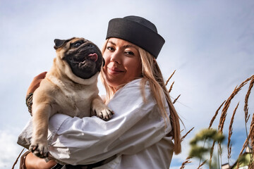 Young happy beautiful woman holding and hugging her beloved dog during a walk with harness and black leash in a city park. Street photography. Favorite pets.