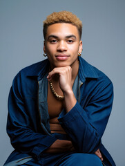 A young man poses confidently with a thoughtful expression, wearing casual attire and jewelry. The studio background enhances his modern fashion look. Generative AI.