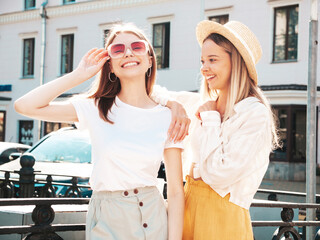 Two young beautiful smiling hipster female in trendy summer clothes.Sexy carefree women posing on the street background in hat. Positive pure models having fun at sunset, hugging