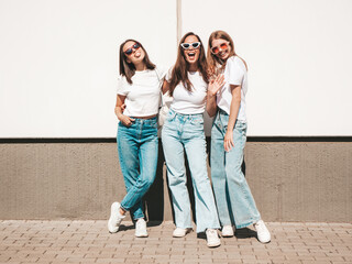 Three young beautiful smiling hipster female in trendy summer same clothes. Sexy carefree women posing on the street background.Positive models having fun in sunglasses.Hugging. Cheerful and happy