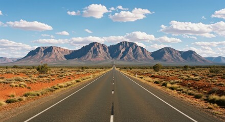Fototapeta premium A long, straight highway cuts through a vast, arid landscape, leading towards majestic mountains under a vibrant blue sky