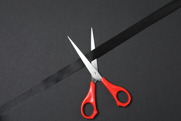 Black ribbon and scissors on black background, flat design. Place for text.
