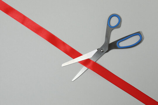 red ribbon and scissors on light grey background, flat lay. space for text
