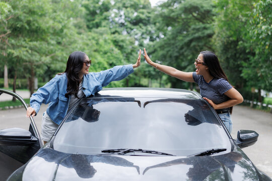 Two happy women giving high five celebrating road trip near car
