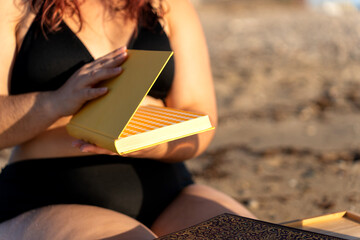 Curvy woman enjoying reading on the beach at sunset