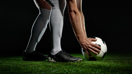 Soccer player in white socks placing ball on green grass with intense posture. Concept of sports...