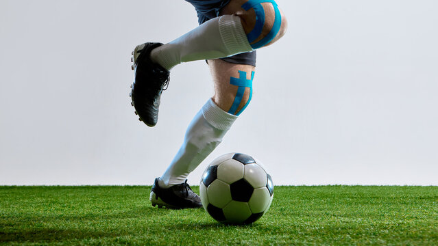 Soccer player with tape on knee getting ready to hit the ball on field. Concept of injury prevention, sports physiotherapy, active recovery, football training, and athletic lifestyle.