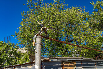 An old, rusty radio and television antenna mounted on a concrete pole next to a dilapidated house,
