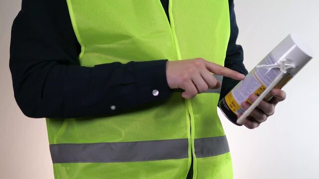 A builder or handyman holds a can of foam in his hands, reads its description and properties. Familiarization with the instructions for using foam materials.