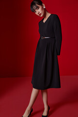 Elegant young woman in black dress against red background.