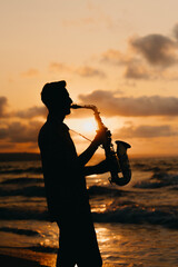 A tranquil and serene silhouette of a talented saxophonist passionately playing at sunset by the...