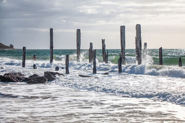 Old wooden jetty ruins on Willunga Beach, South Australia, with turquoise ocean and foamy waves