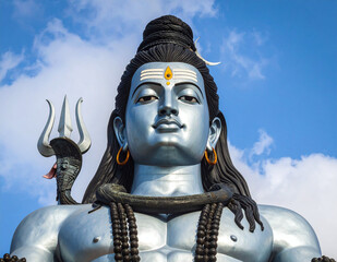 Imposing Lord Shiva idol featuring snake and trident with spiritual calm against blue cloudy sky and divine symbolism