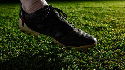 Close-up of soccer cleat pressing into grass on field under spotlight. Concept of football tension,...