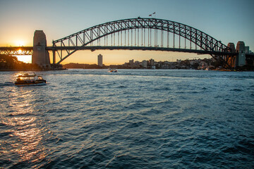 Sydney Harbour Bridge at sunset with boats on the water and city skyline in background