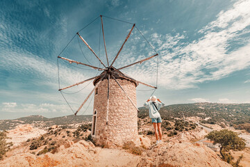 Traveler admiring a historic stone windmill under a bright sky, surrounded by a picturesque...