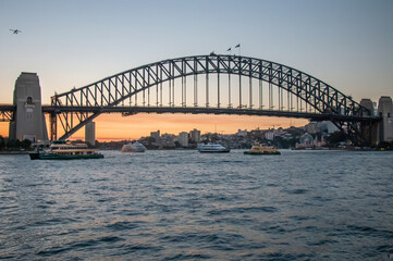 Fototapeta premium Sydney Harbour Bridge at sunset with boats on the water and city skyline in background
