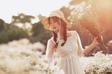 Young woman in white dress holding flowers in the sunny field.