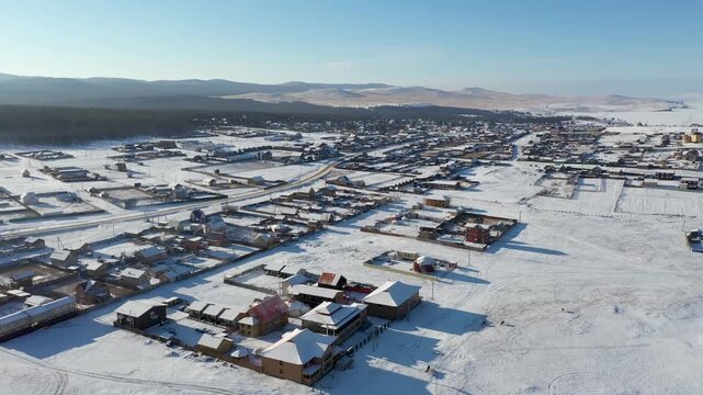 Aerial view of Khuzhir village shows a blanket of white snow covering houses and landscape, contrasting against the clear blue sky, Khuzhir, Irkutsk Oblast, Russia.
