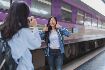 Young tourists taking photos at train station with thumbs up