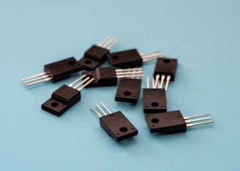 Close-up of multiple black electronic transistors with three metal pins on a blue background