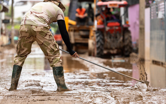 Thai workers cleaning a mud-covered street after a major flood. Wearing safety gear, they work together to restore public roads, showing resilience and community effort in disaster recovery
