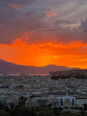 Spectacular fiery red sunset over Cagliari city, Sardinia - Panoramic view of urban skyline at dusk with golden reflections on Mediterranean Sea. 