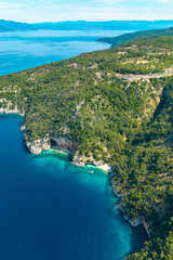 Fototapeta premium Aerial view of lush green hills and rocky coastline meeting turquoise waters on Cres Island. Secluded coves, boats, and a cave create a dreamy Mediterranean escape