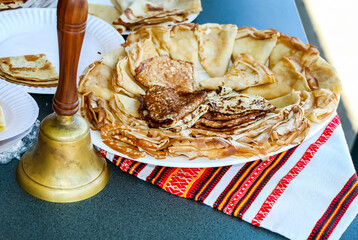 Traditional Russian homemade pancakes served on plates with festive cloth and brass bell at food celebration