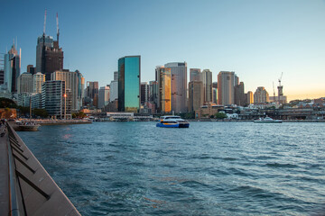 Modern skyline of Sydney city at sunset with ferry in foreground and waterfront buildings
