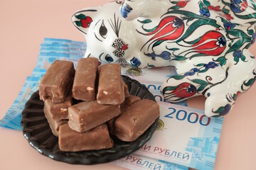 A ceramic toy cat. Next to it is a plate of sweets and paper bills. Russian rubles.