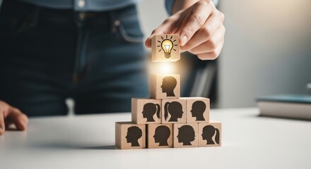 Hand placing a lightbulb on a pyramid of people silhouette blocks