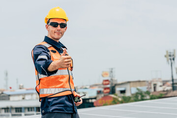 Construction worker wearing helmet and safety gear inspecting solar panels on a rooftop in an urban...
