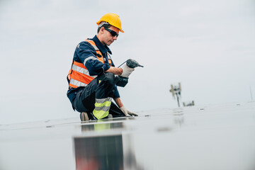 Worker repairs solar panels on rooftop during daytime while wearing safety gear