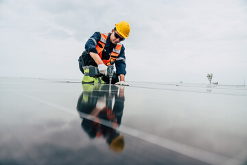 Worker installs solar panels on a building roof under a cloudy sky during the daytime while using a power tool