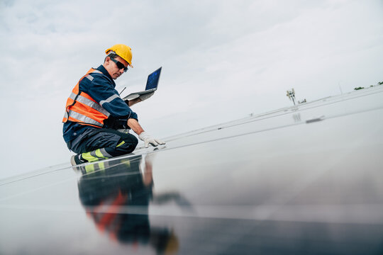 Solar panel technician performs maintenance on a rooftop installation while using a laptop for monitoring and diagnostics
