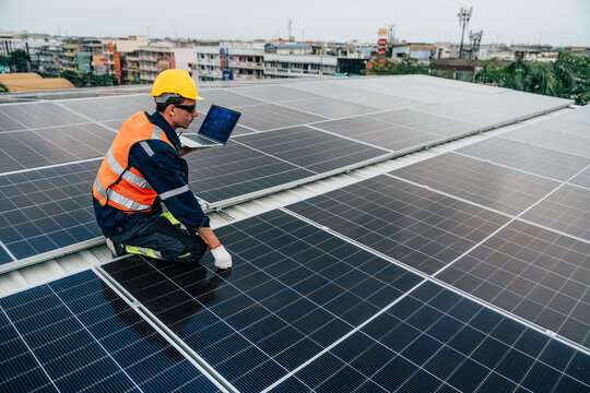 Technician inspects solar panels on rooftop while using laptop for data analysis in urban area