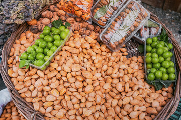 Wicker basket overflowing with fresh almonds, walnuts, plums and dried apricots at a farmers market, healthy and nutritious snack