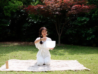 Chinese woman meditating with Tibetan singing bowl Outdoors. Yoga practice in sunny day. Spiritual...